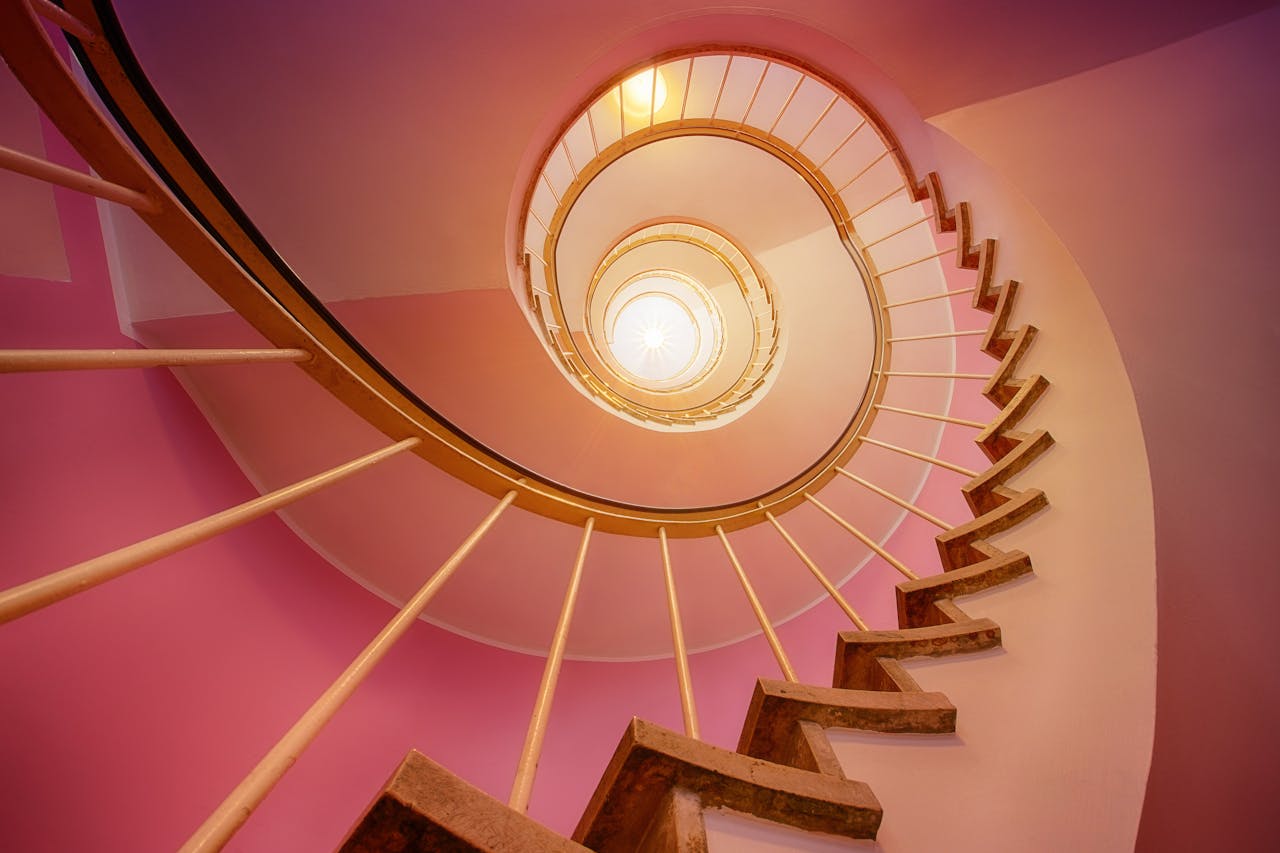 Stunning upward view of a spiral staircase with pink and gold hues, creating a modern art ambiance.